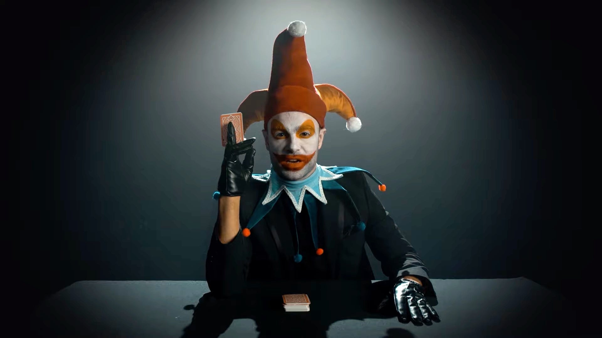 A man in a clown outfit plays with cards.