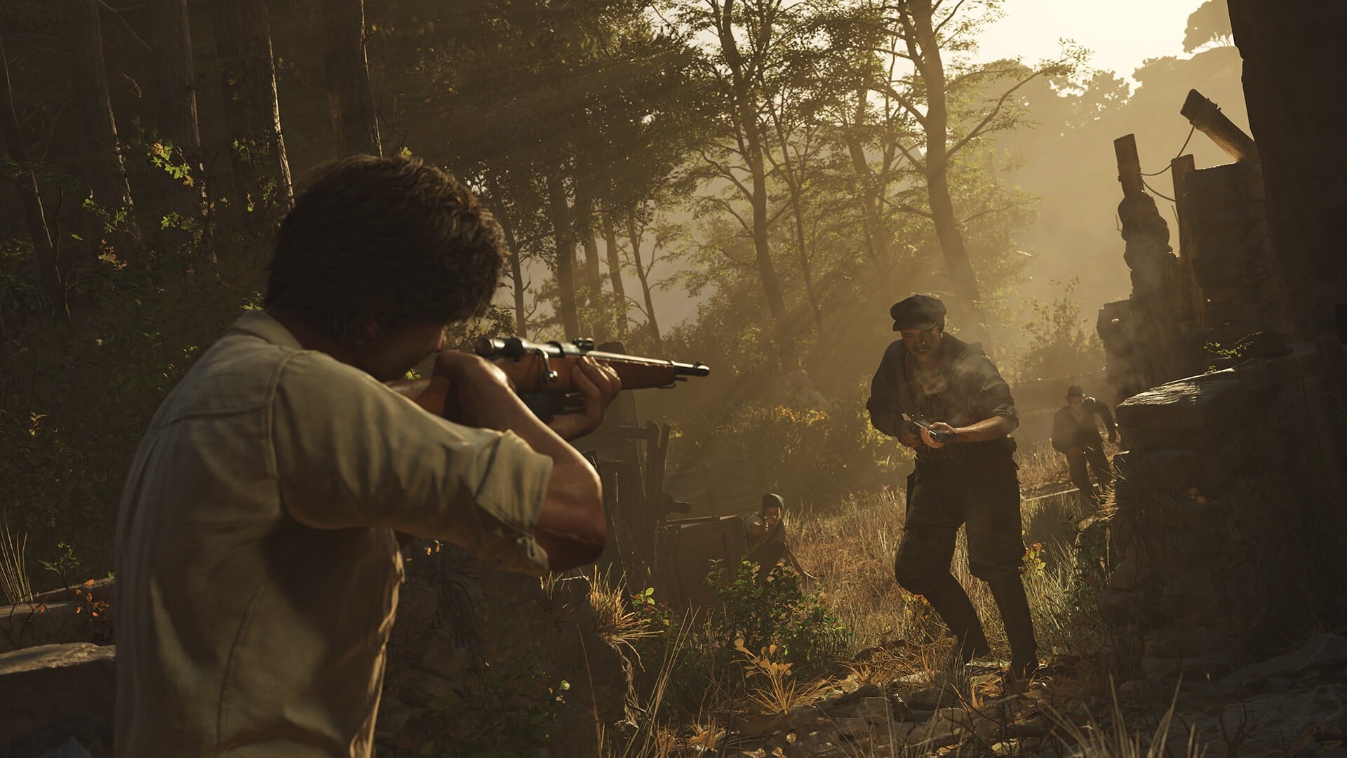 A screenshot of Mafia: The Old Country gameplay shows a man in the foreground pointing a rifle at another man who is antagonistically approaching him in a sun-dappled Sicilian environment.