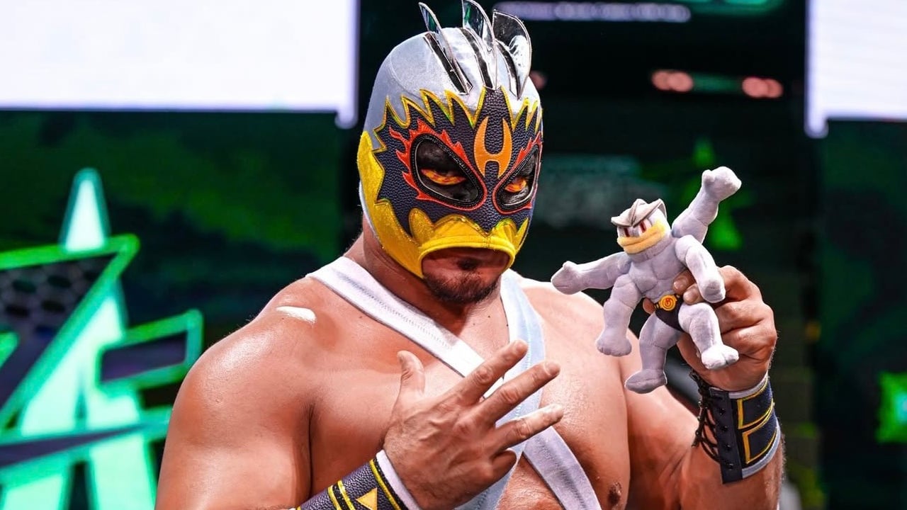 A wrestler in a Machamp-themed costume holds a Machamp plush.