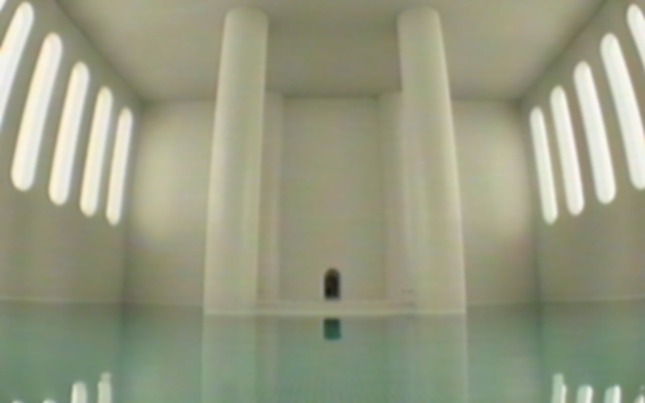 A pool reflects light in a massive empty room while a dark doorway lies ahead.