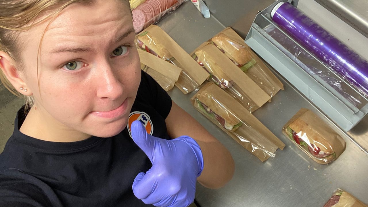 7licious gives a thumbs up to the camera while she makes sandwiches.