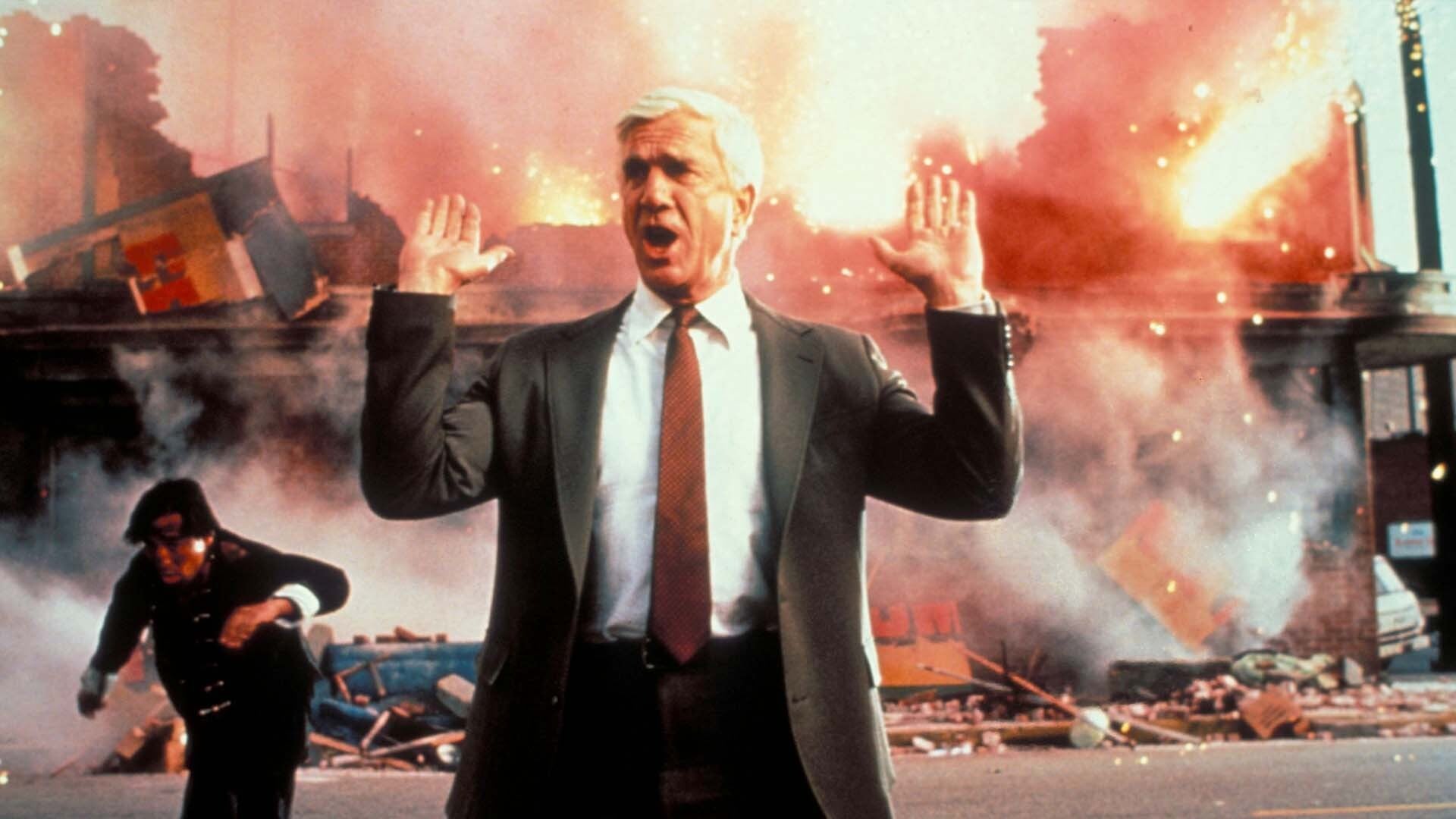 A man holds up his hands as things explode.